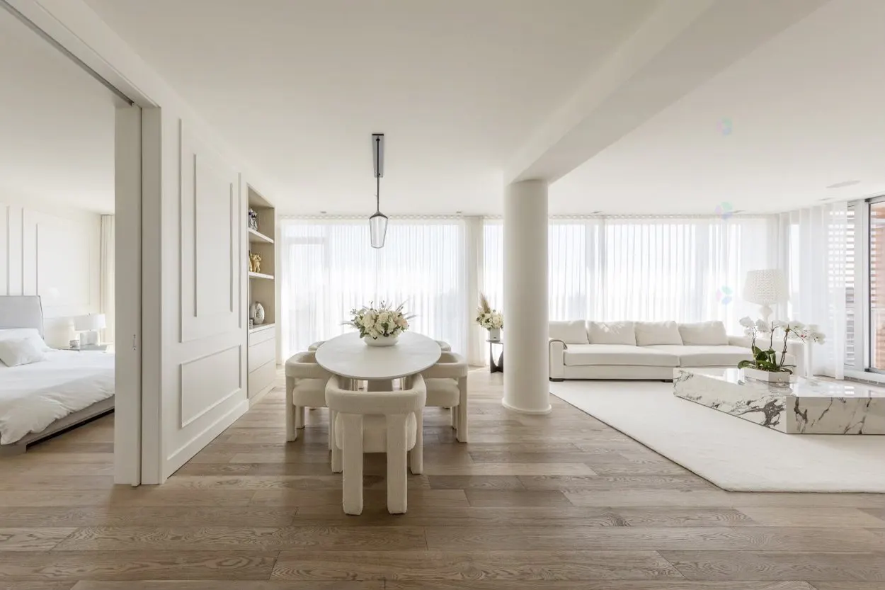 Bright, open-concept living area with white furniture, marble coffee table, dining set, and hardwood floors.