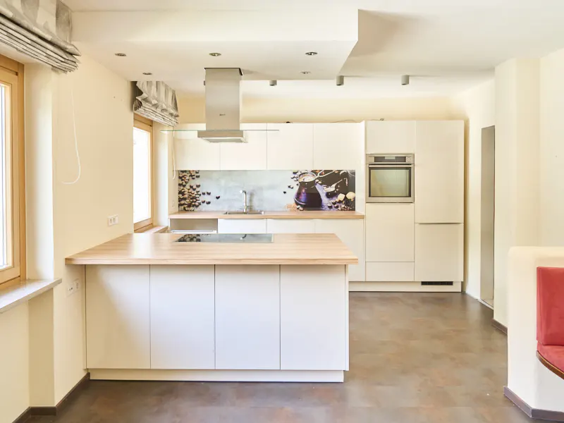 Bright kitchen with white cabinets, a wood-topped island, and a stainless steel range hood. A coffee-themed backsplash adds a decorative touch.