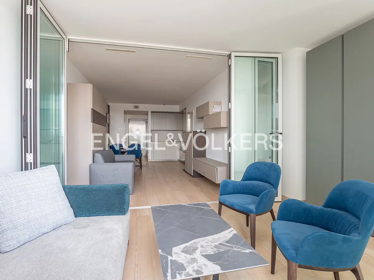 Living room with blue chairs, gray sofa, marble table, and open glass doors to a kitchen.