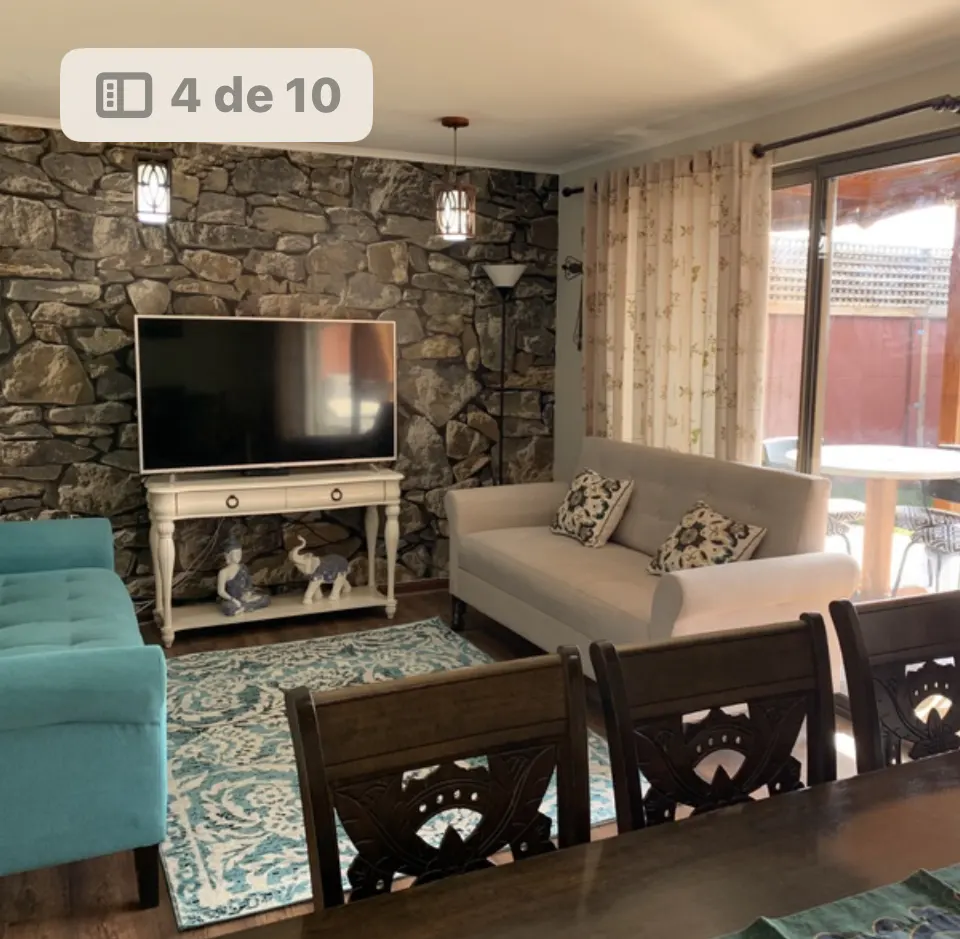 Living room with stone wall, TV, white sofa, blue chaise lounge, patterned rug, and dining table with chairs.