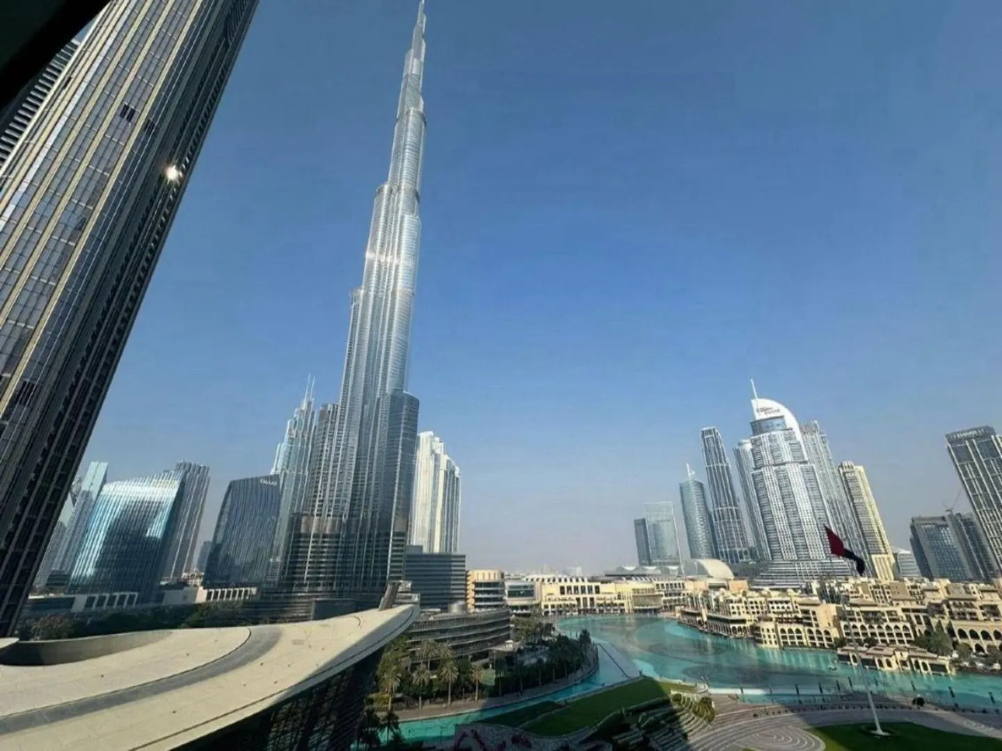 Dubai skyline view featuring the Burj Khalifa, modern buildings, and a turquoise water feature under a clear blue sky.