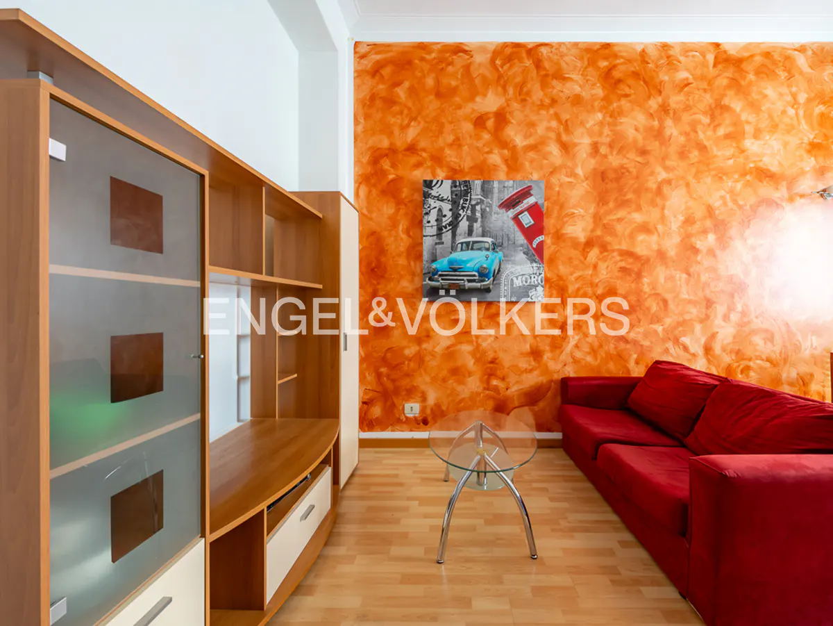 Living room with orange textured wall, red sofa, glass table, and wood entertainment center. A vintage car print hangs on the wall.