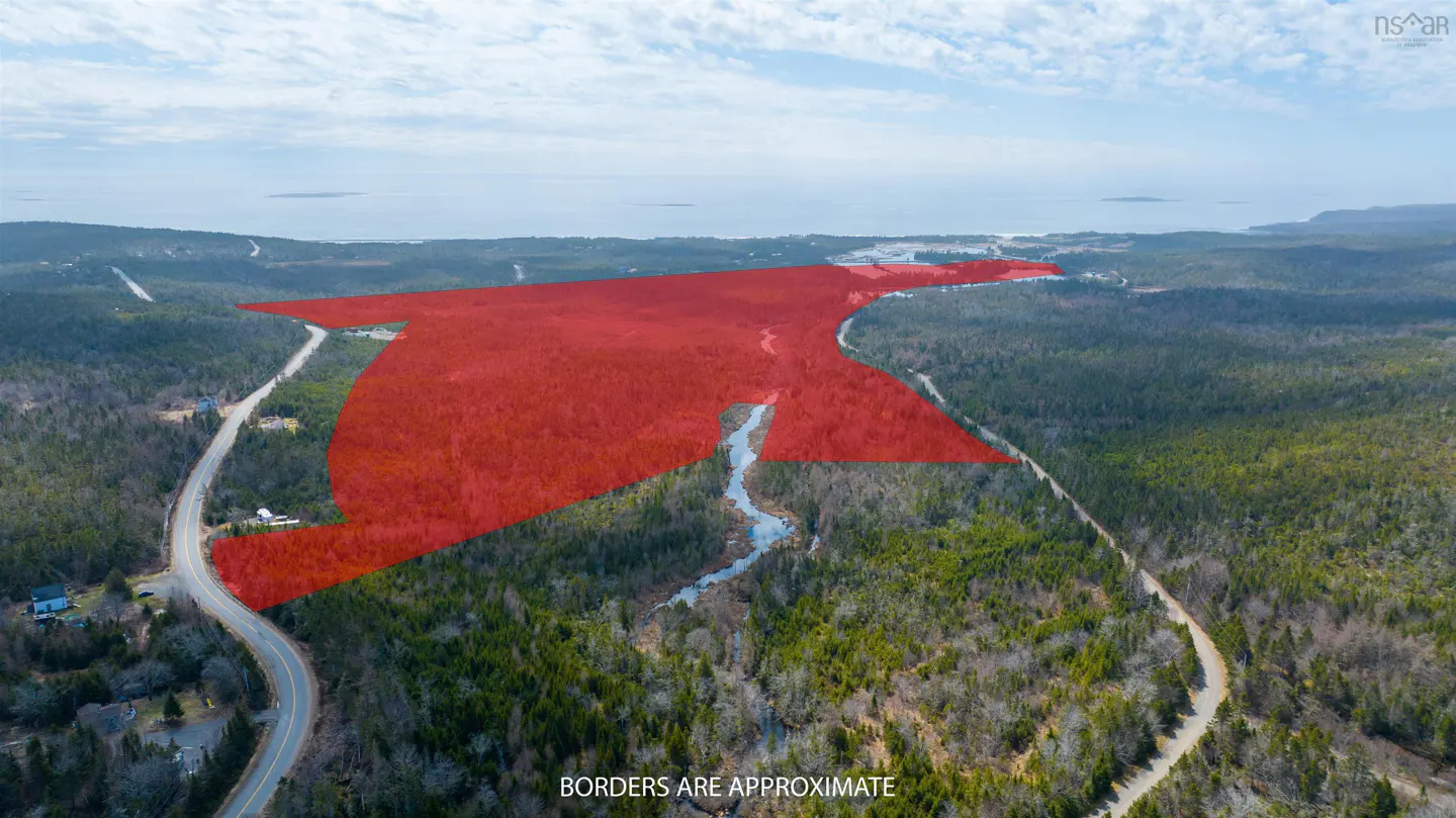 Aerial view of land for sale, outlined in red, surrounded by green trees, a winding road, and a river. Ocean in the background.