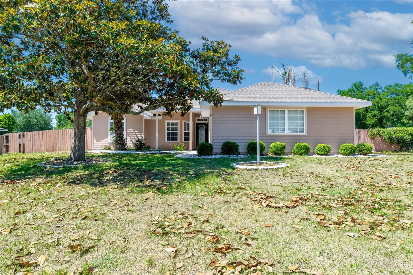 A tan single-story house with a large tree in the front yard.