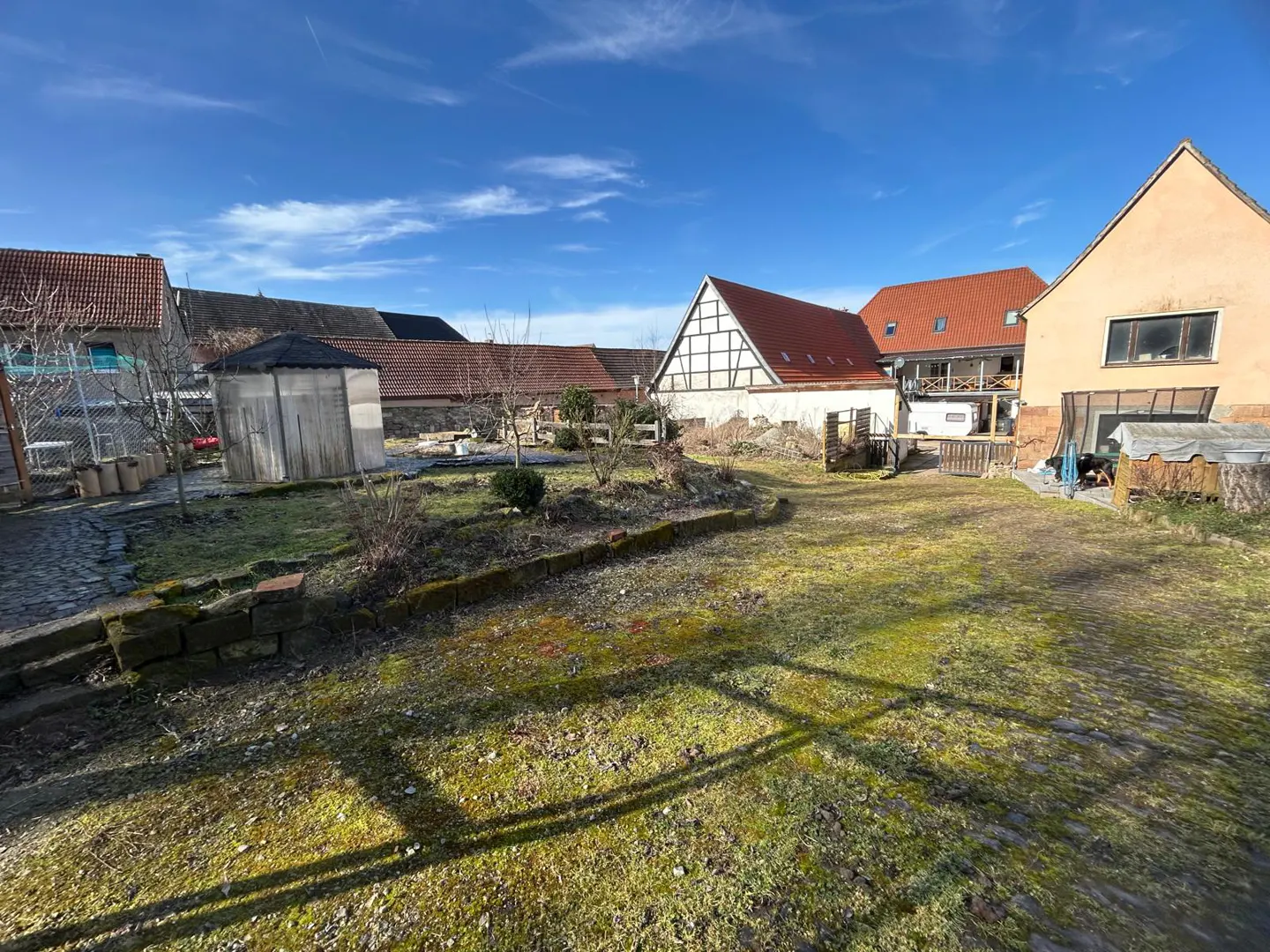 Exterior shot of a large yard with grass, stone walls, and several buildings with red tile roofs under a blue sky.