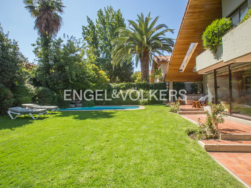 Lush green lawn with pool, lounge chairs, and palm trees. House with wood trim and large windows in the background.
