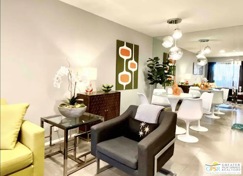 Living room with gray walls, a yellow sofa, a gray chair, a glass table, and a dining table with white chairs.