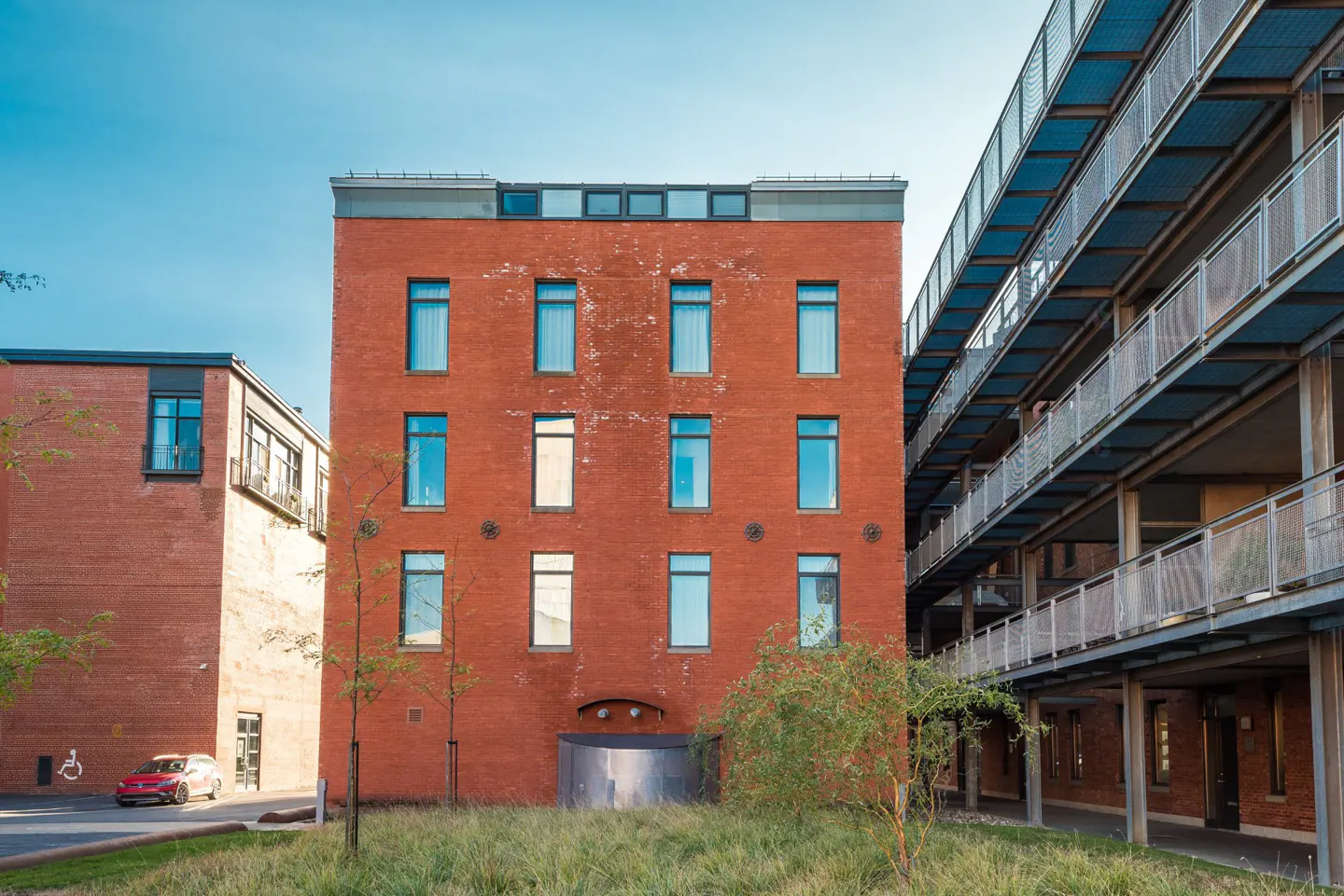 Exterior view of a red brick apartment building with blue-trimmed windows and a metal balcony structure on the right.