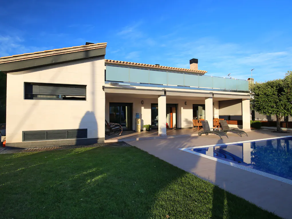 Modern white house with a pool, lawn, and blue sky. Lounge chairs sit on the patio.