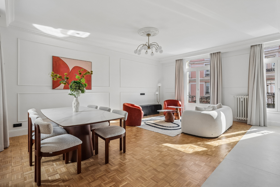 Bright living and dining room with parquet floors, white walls, a marble dining table, and a curved white sofa. [AI-generated text]
