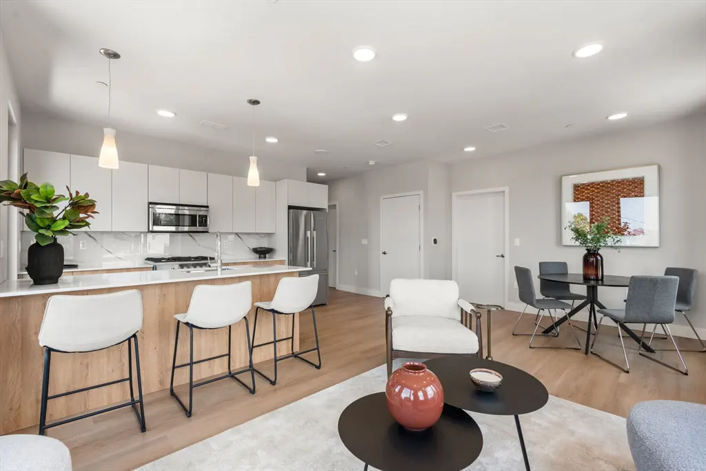 Open-concept living space with a kitchen island, white cabinets, and stainless steel appliances. A dining table and chairs are visible.
