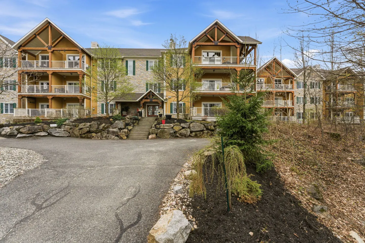 Exterior view of a multi-story condo building with balconies, stone accents, and a landscaped entrance.