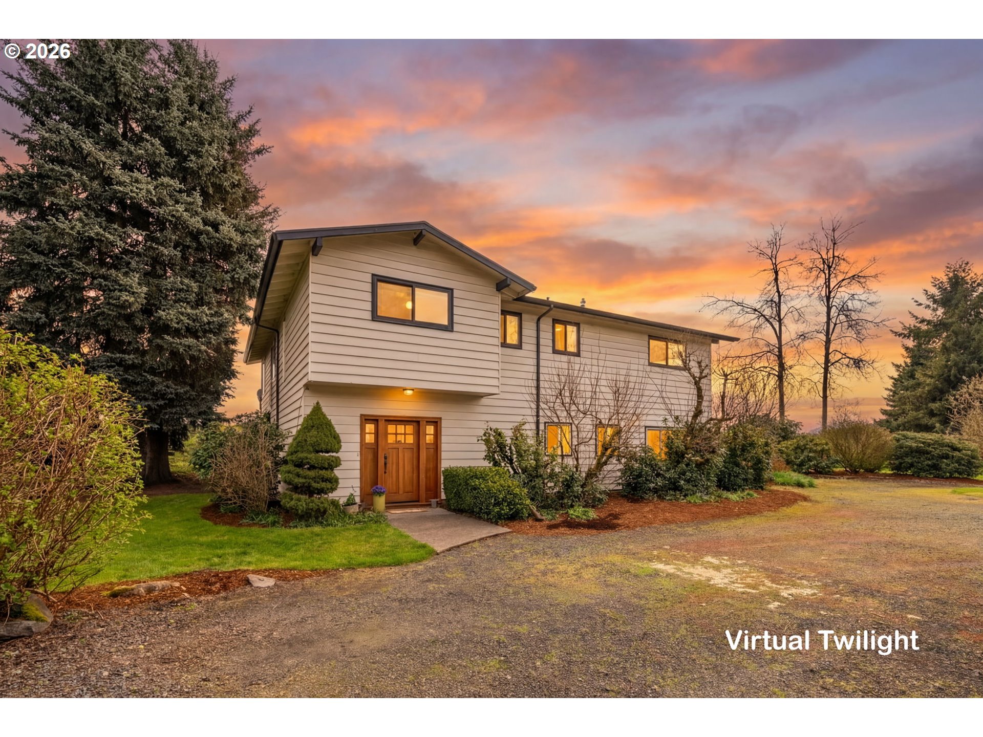 Two-story beige house with a wooden front door at twilight, set against a vibrant orange and purple sunset sky.