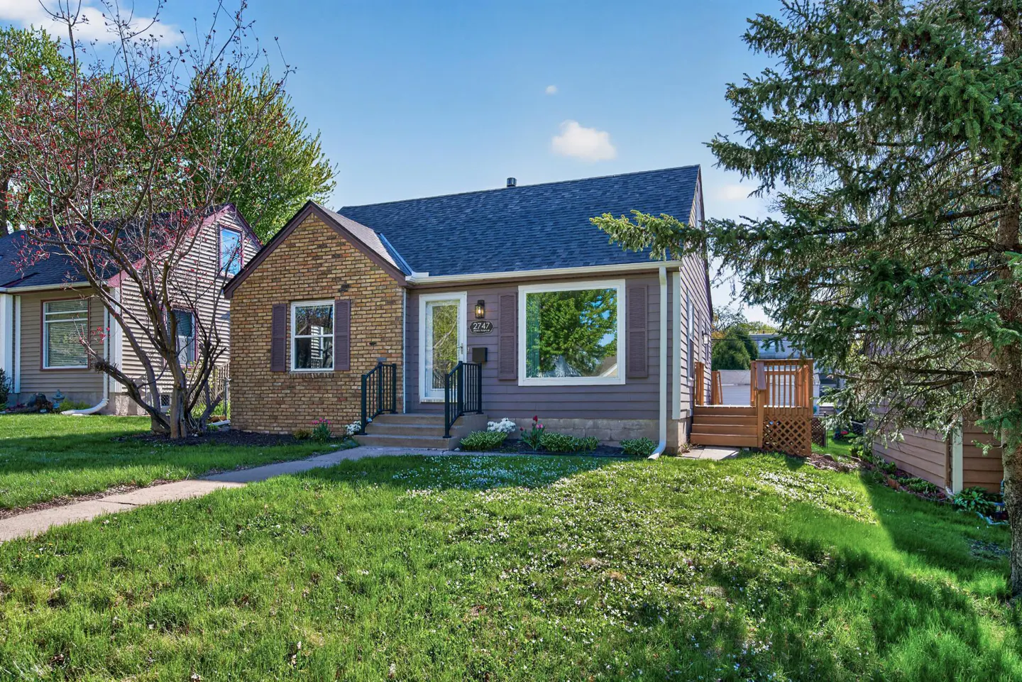 A single-story home with a brick and brown siding exterior, a blue roof, and a green lawn under a blue sky.