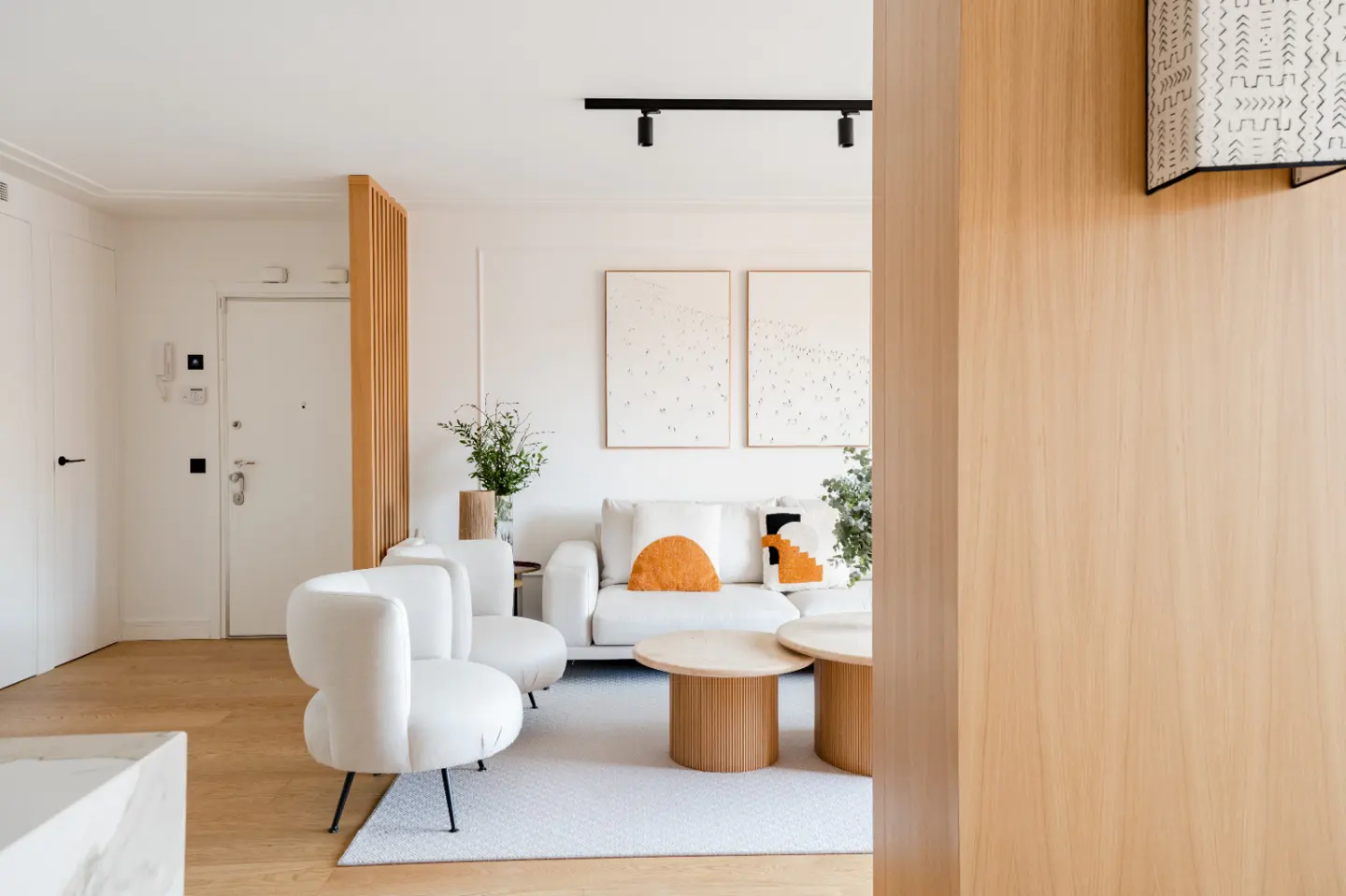 Bright living room with white sofa, chairs, and rug. Two round wooden tables sit in front of the sofa. Two framed prints hang on the wall.