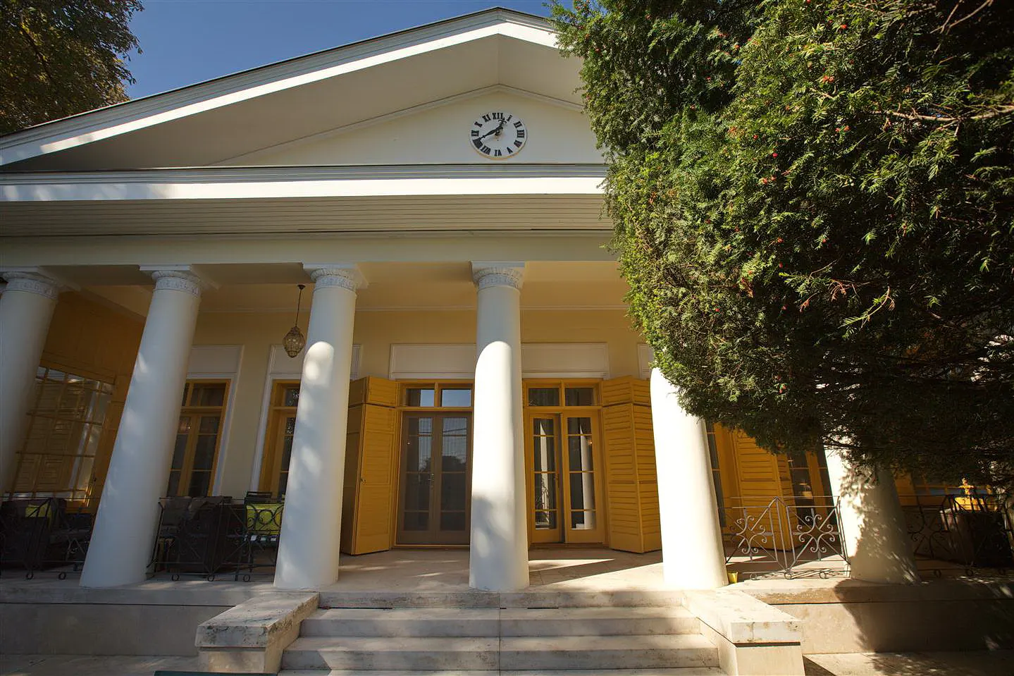 Exterior of a yellow house with white columns and a clock above the entrance.