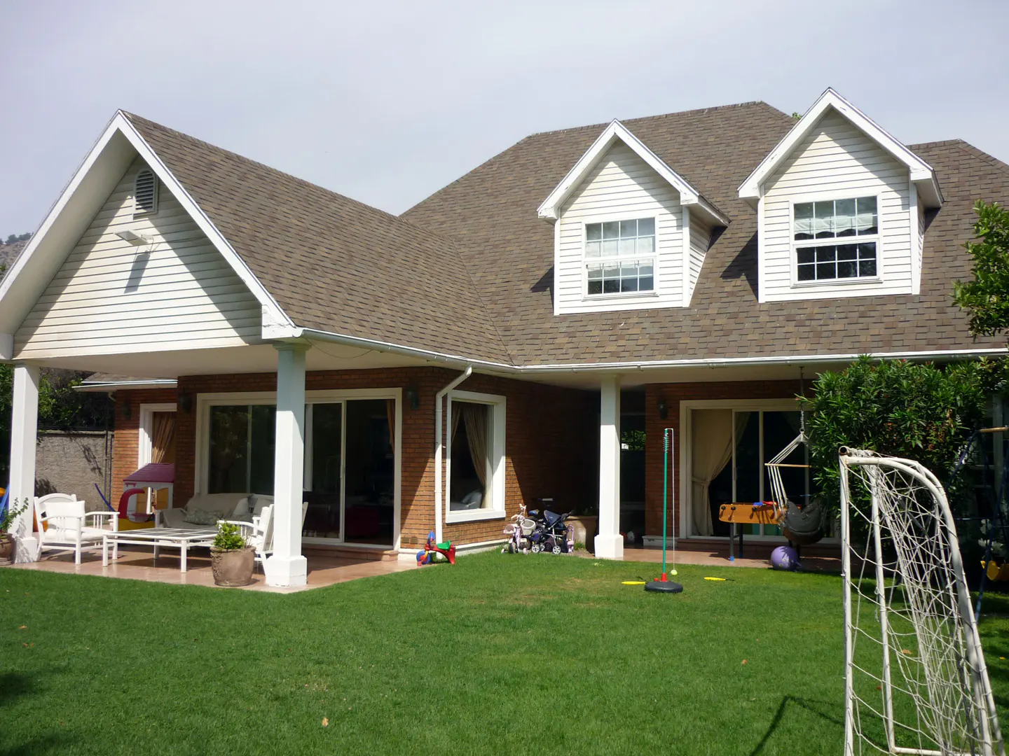 Backyard view of a two-story house with a brown roof, white siding, and a green lawn with toys and a soccer goal.