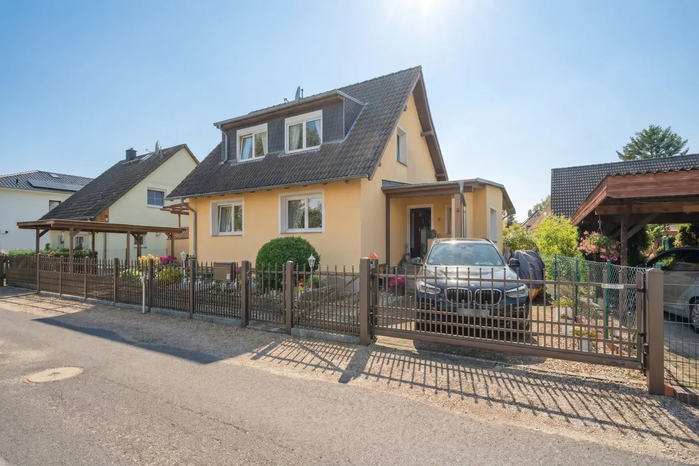 Two-story yellow house with a dark gray roof, a brown fence, and a black car parked in front.