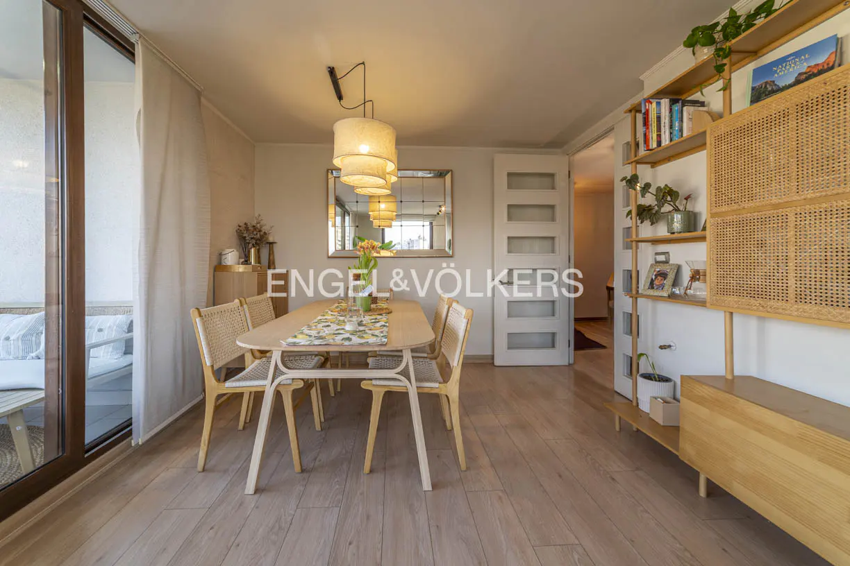 Bright dining room with wood floors, table with four chairs, and a bookshelf with plants and books. A sliding glass door leads to a balcony.