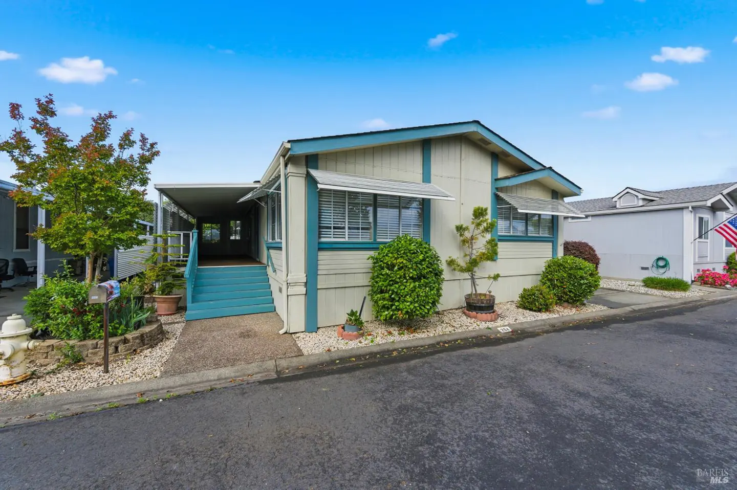 A light green mobile home with blue trim, a covered porch, and a blue staircase under a bright blue sky.