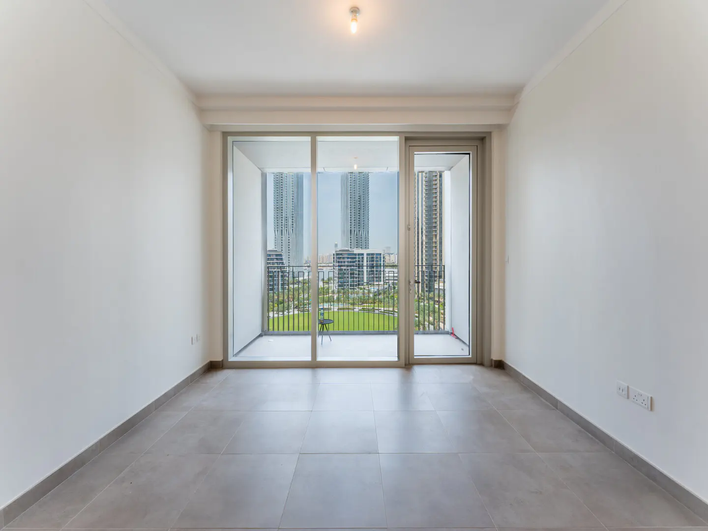 Empty room with gray tile floor and white walls. Sliding glass doors lead to a balcony with a city view.