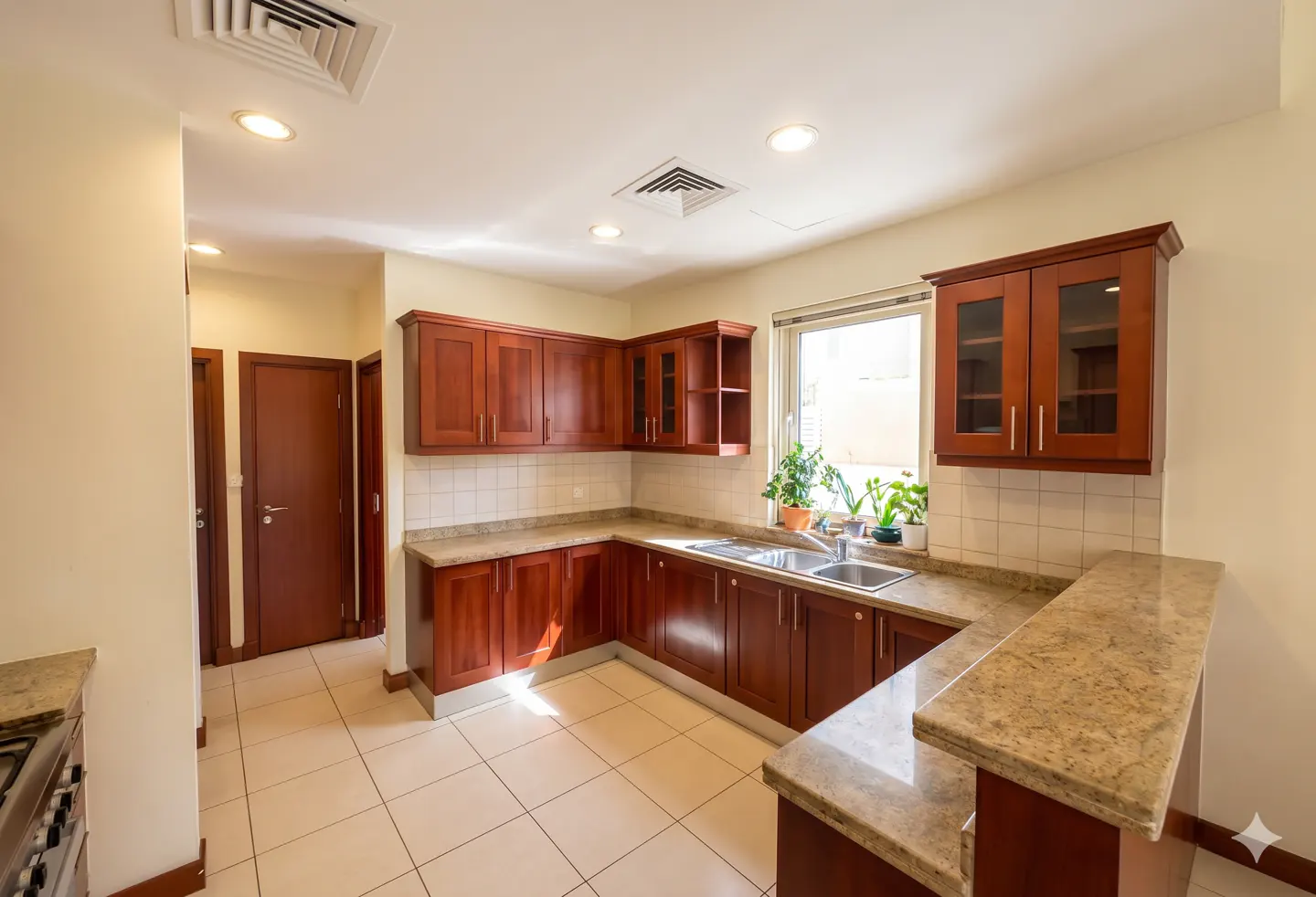 L-shaped kitchen with cherry wood cabinets, beige granite countertops, tiled floors, and a window with potted plants.