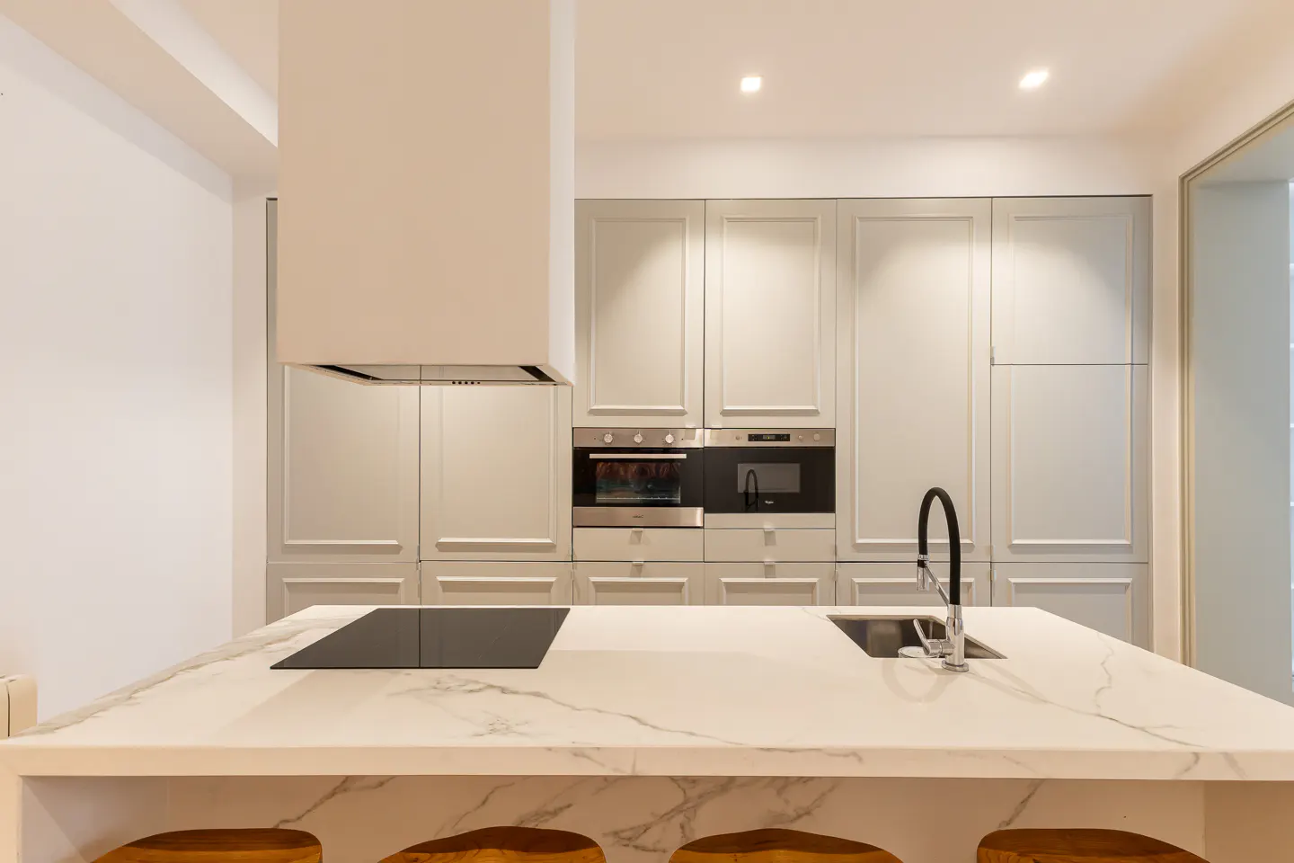 A modern kitchen with gray cabinets, stainless steel appliances, and a white marble island with wooden stools.