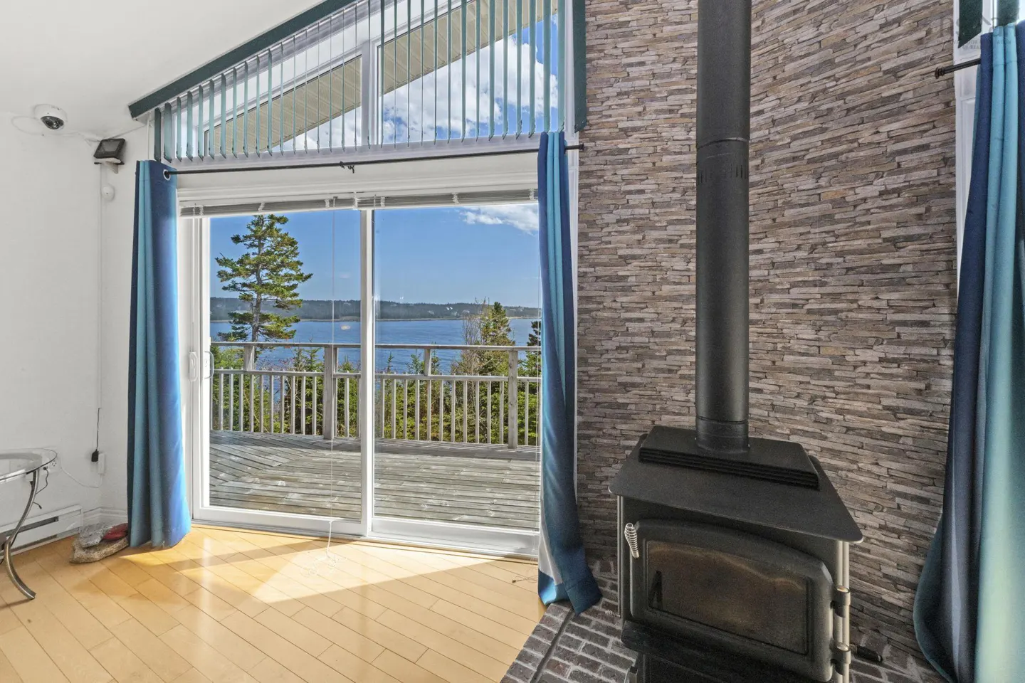 Living room with a wood stove, stone accent wall, and sliding glass doors opening to a deck with a scenic water view.
