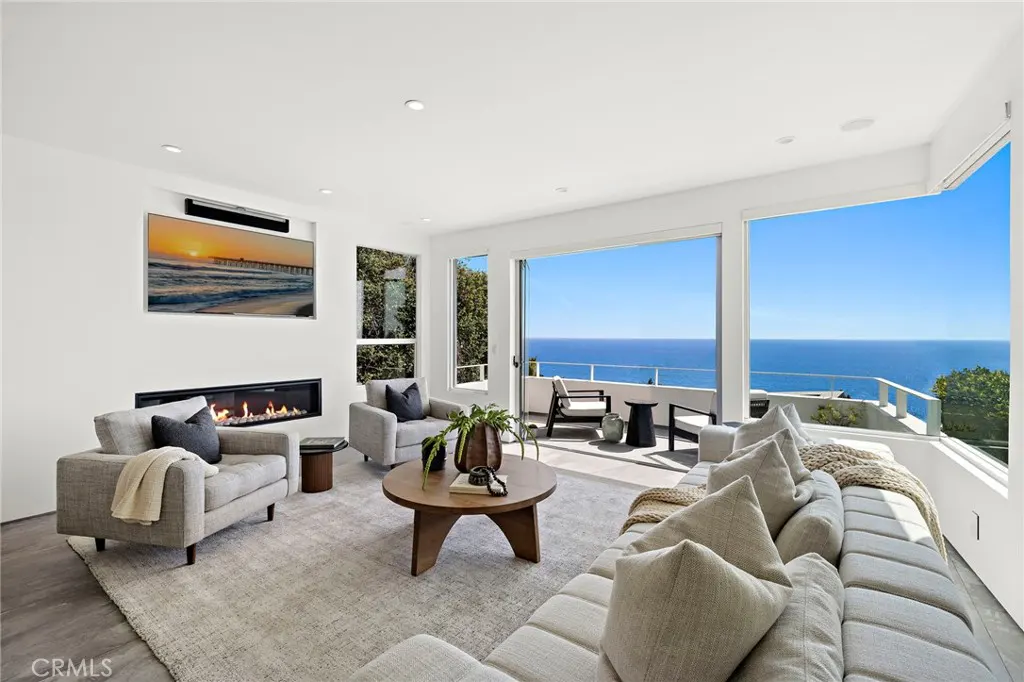 Modern living room with fireplace, neutral furniture, and floor-to-ceiling windows overlooking the blue ocean.