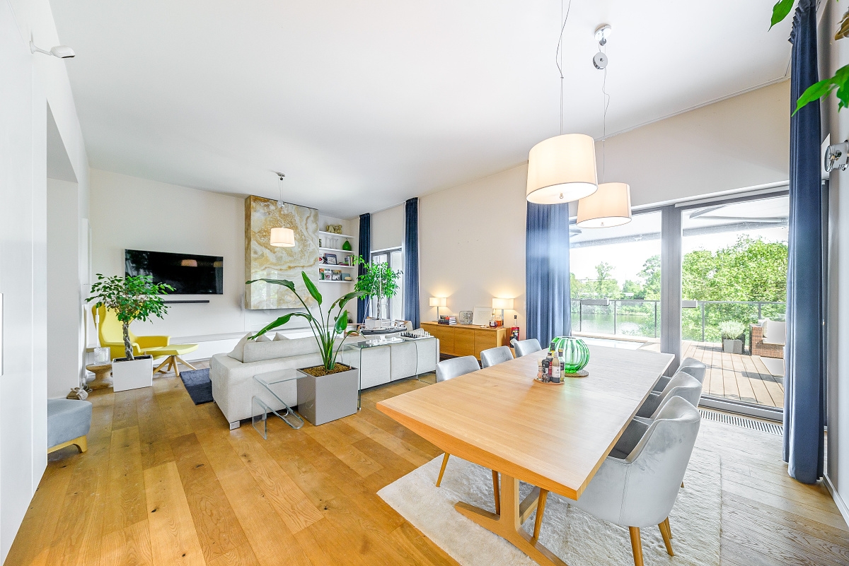 Bright open-plan living and dining room with hardwood floors, a white sofa, a wooden dining table, and a balcony view. [AI-generated text]