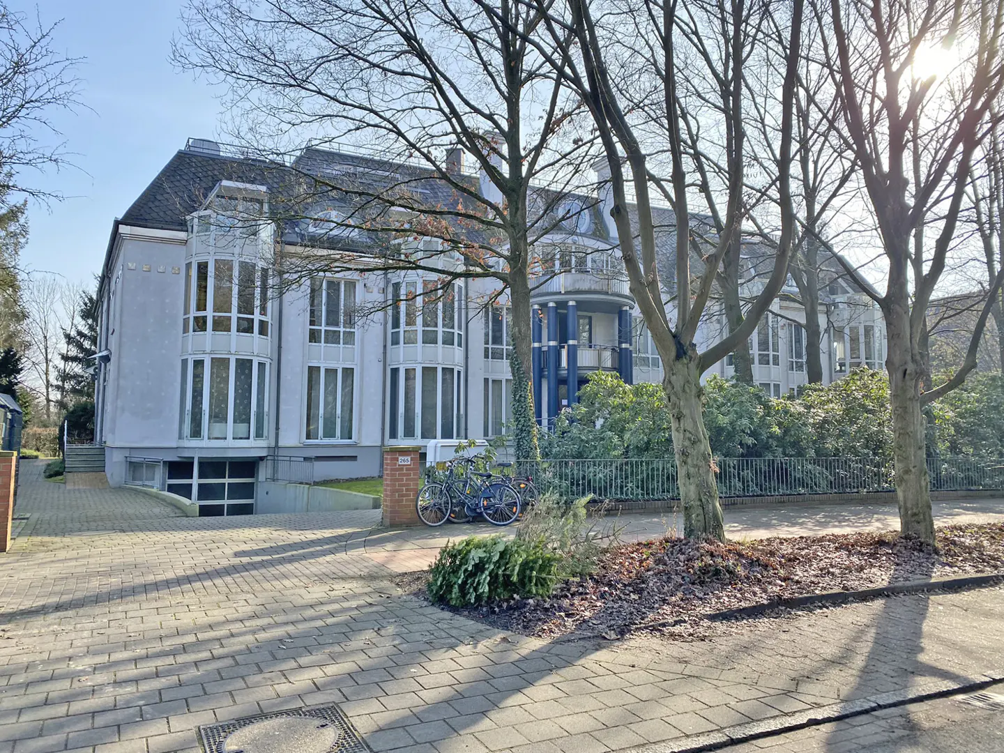 A two-story gray building with many windows, a blue balcony, and two bicycles parked outside.