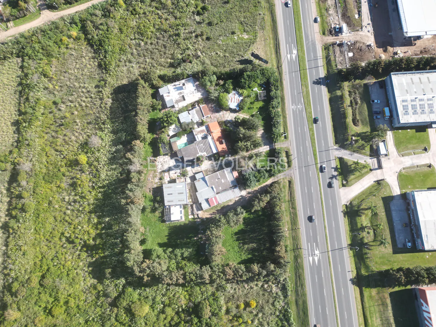Aerial view of houses nestled between green foliage and a highway with moving cars.