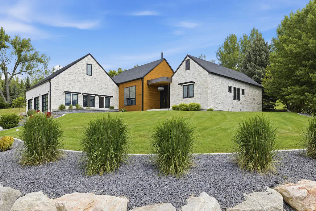 Exterior of a modern home with white stone and wood siding, black trim, and a green lawn.