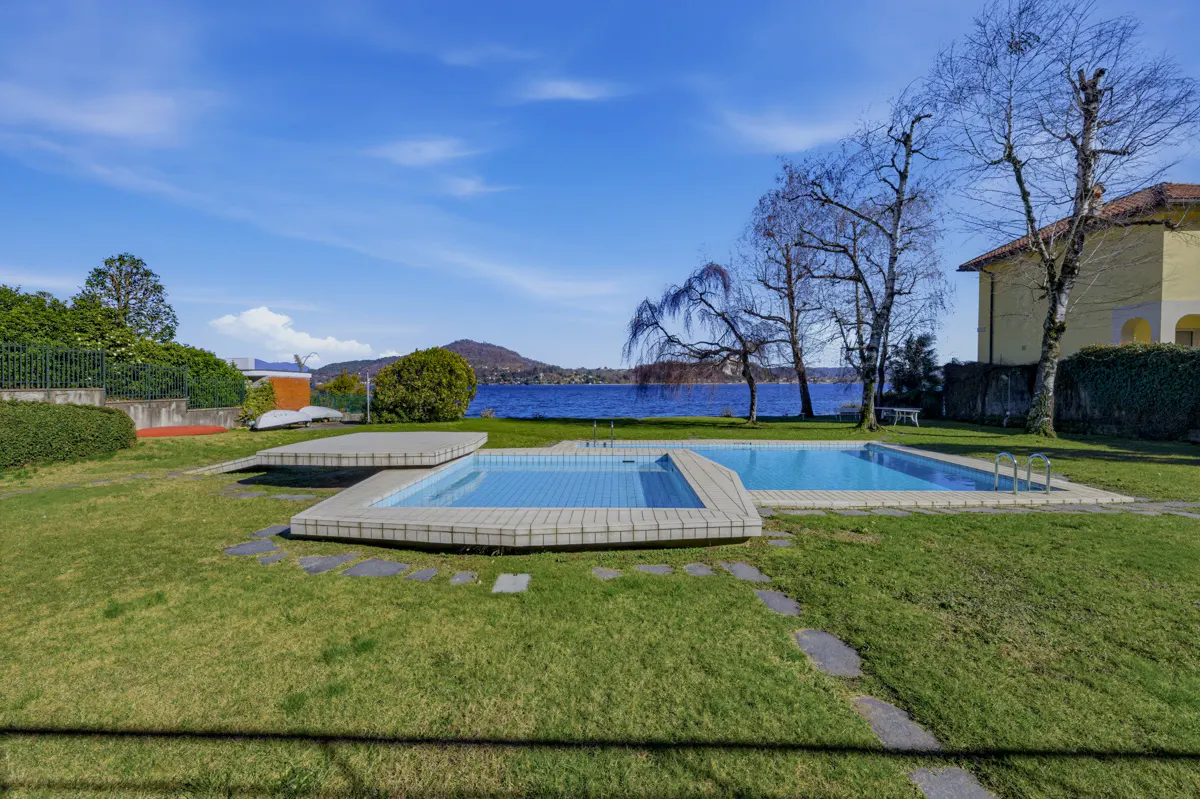 Outdoor pools on a green lawn, with a lake and mountains in the background under a blue sky.