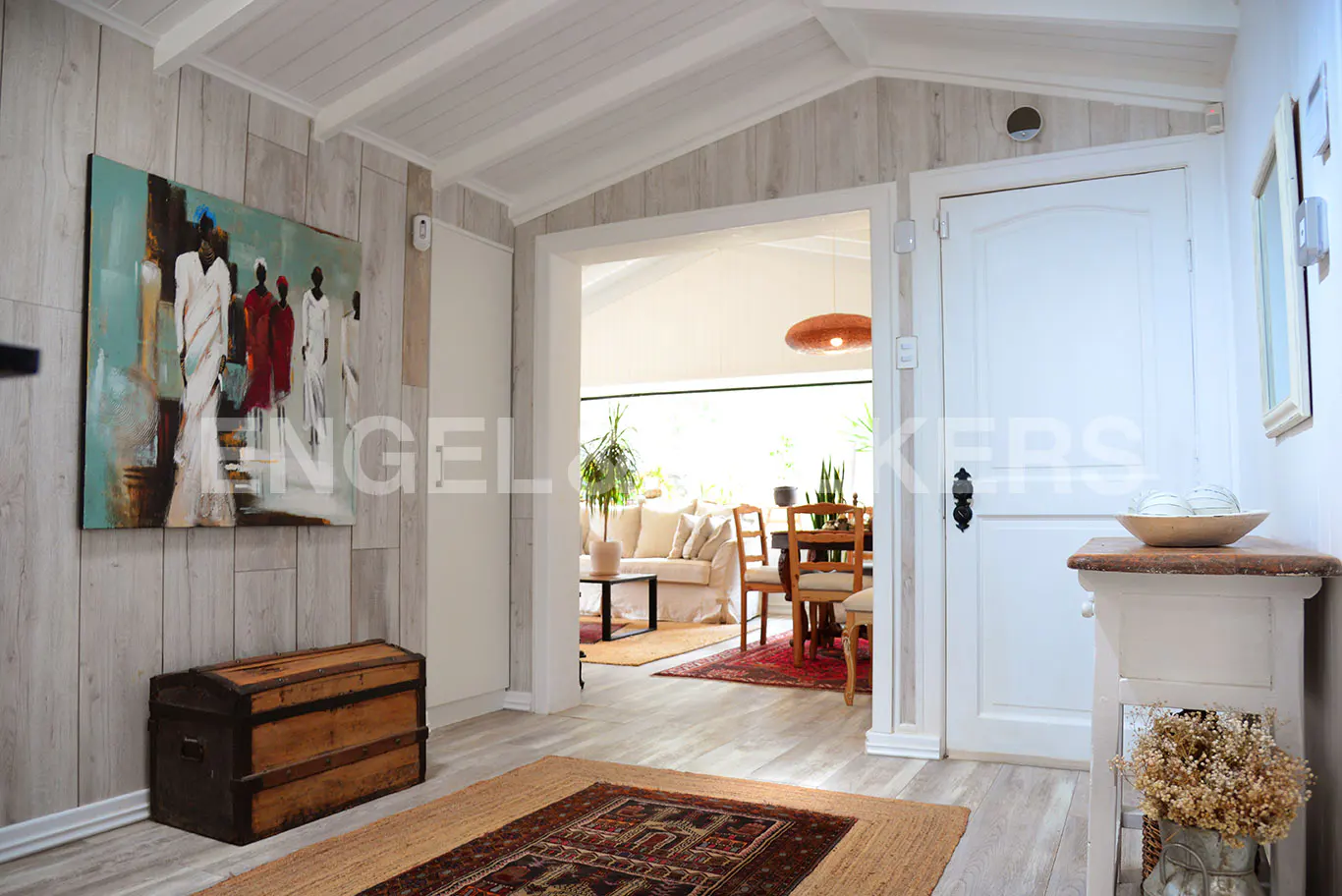 A bright home entryway with a painting, a trunk, and a view into a living room.