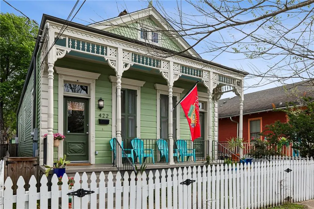 Exterior of a light green house with white trim, a porch with blue chairs, and a white picket fence.