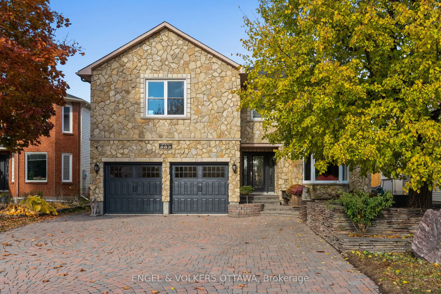 Two-story stone house with a brick driveway and two-car garage on a sunny day.