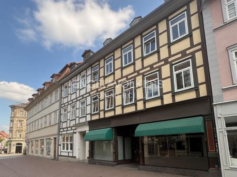 A three-story half-timbered building with cream walls, dark brown beams, and green awnings over ground-floor storefronts. [AI-generated text]