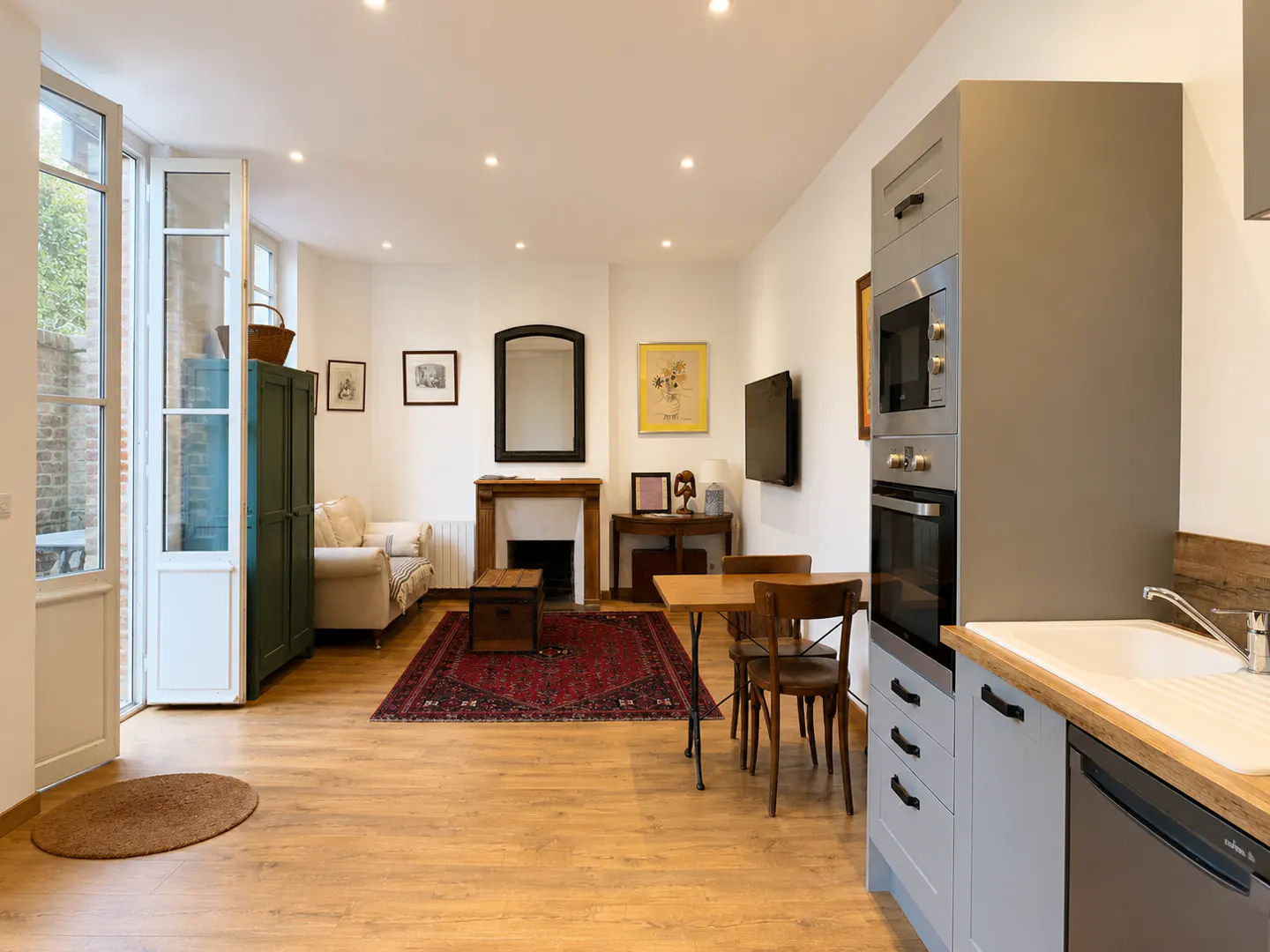 Open-plan living area with a modern grey kitchen, dining table, and a cozy lounge with a fireplace and red area rug.