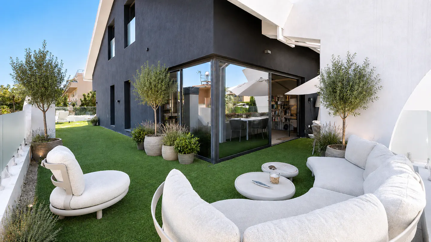 Modern terrace with artificial grass, white curved outdoor sofas, potted trees, and a black house exterior with glass walls.