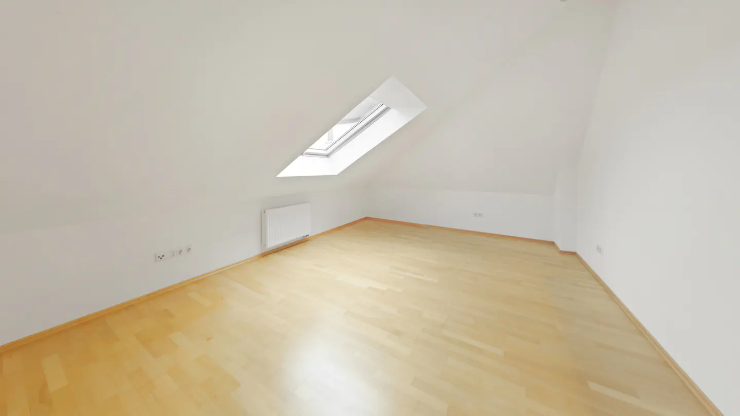 Attic room with light wood floor, white walls, and a skylight. A radiator is on the wall.