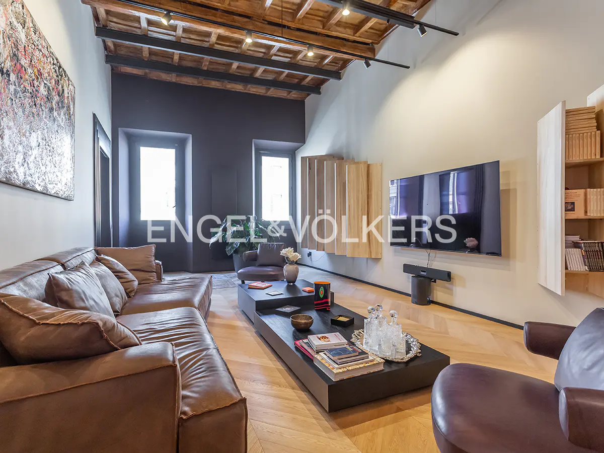 Modern living room with brown leather sofa, black coffee table, wall-mounted TV, and exposed wooden beam ceiling.