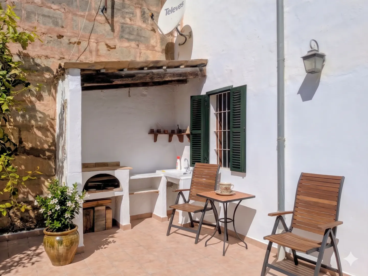 Outdoor patio with a grill, sink, table, and chairs. The walls are white, and there is a satellite dish on the roof.
