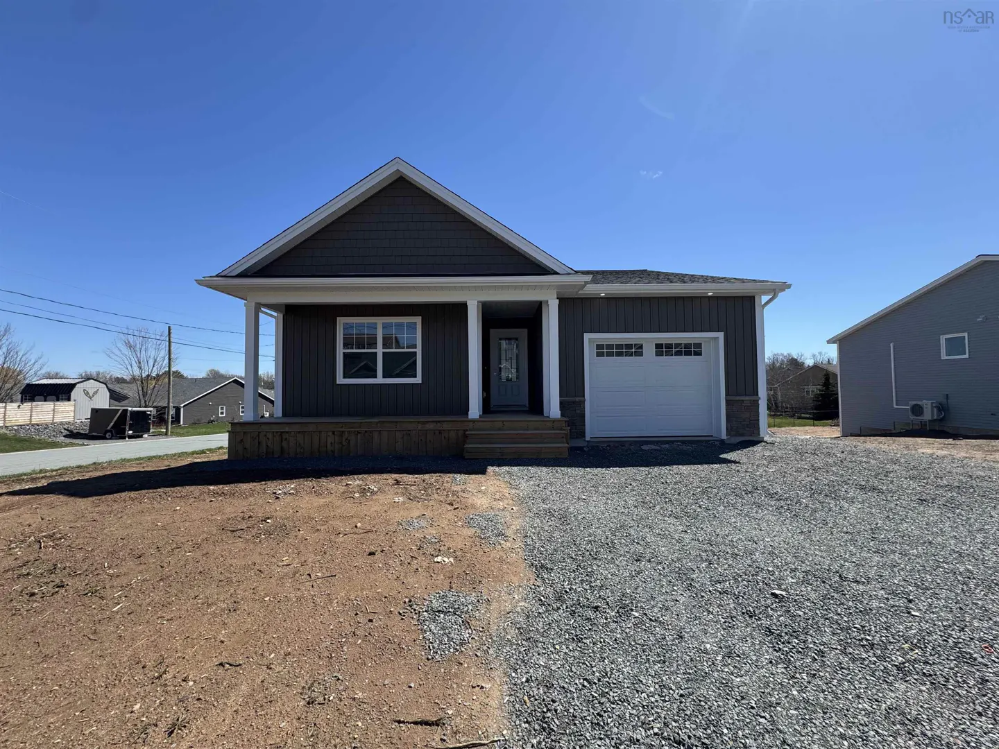 A single-story house with gray siding, a white garage door, and a small porch. The yard is gravel and dirt.