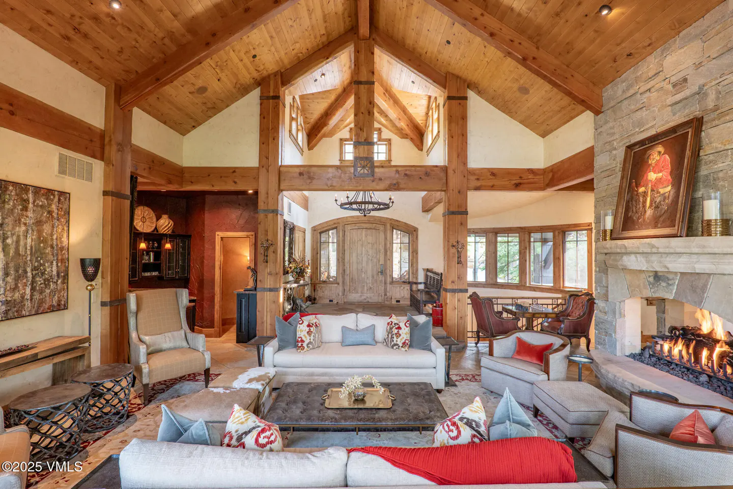 A spacious living room with a stone fireplace, wood beams, and white sofas.