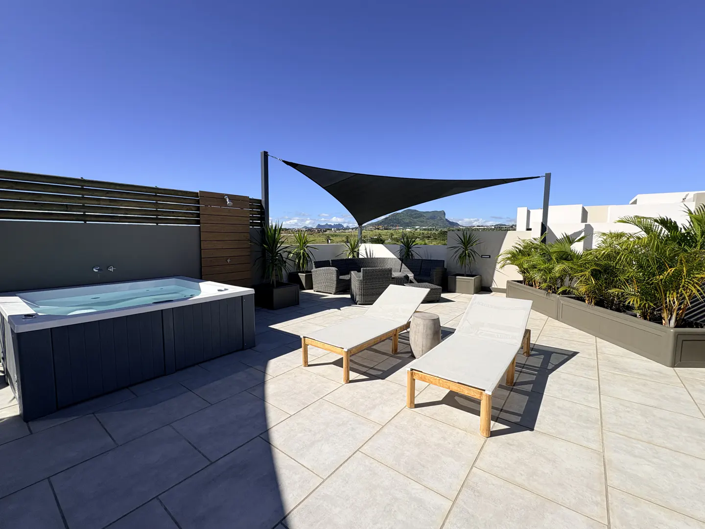 Rooftop patio with a hot tub, lounge chairs, and seating area under a shade sail, with mountain views.