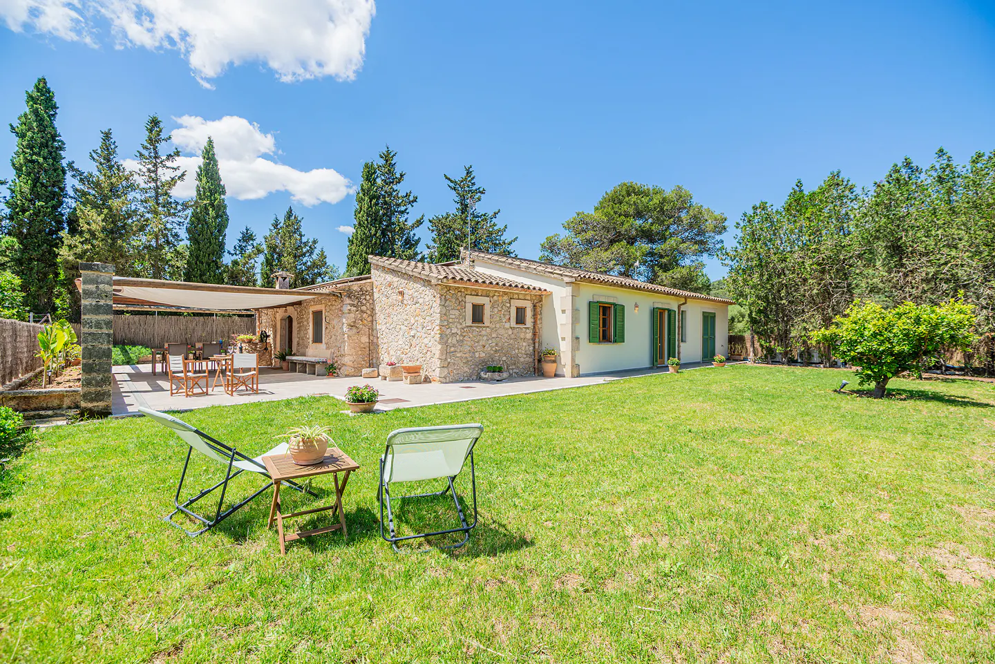 Exterior of a stone house with green shutters, a lawn, and two lawn chairs.
