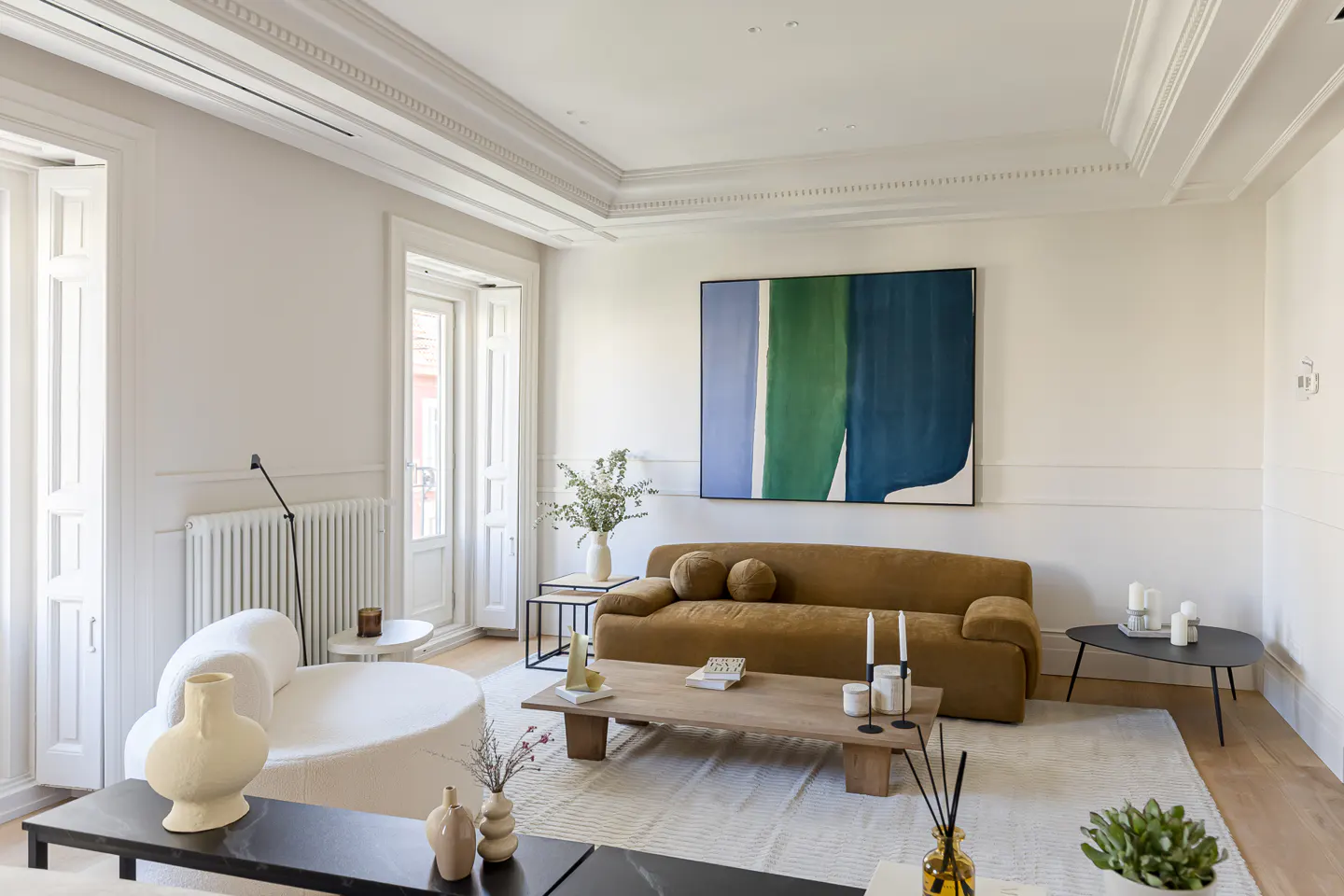 Bright living room with white walls, a brown sofa, and a large abstract painting with green and blue colors.