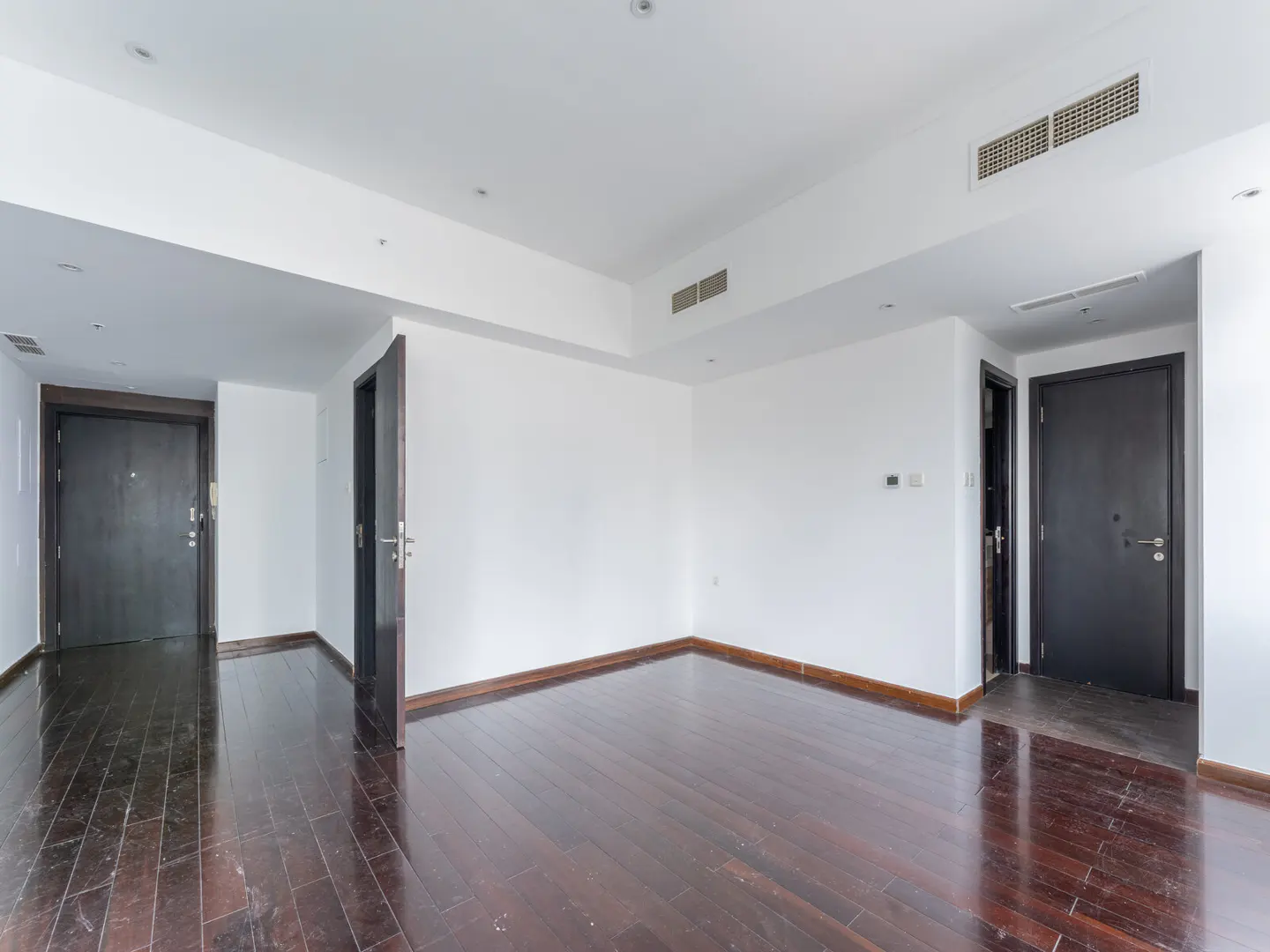 Empty room with dark wood floors, white walls, and two dark doors. One door is slightly ajar.