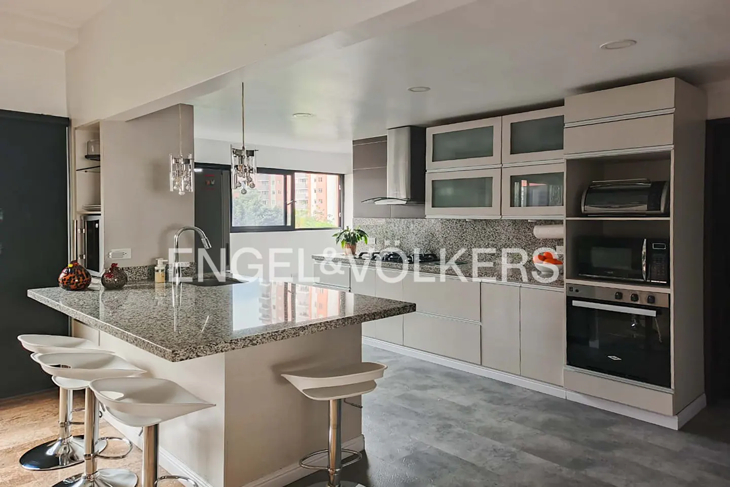A modern kitchen with gray cabinets, granite countertops, and white bar stools at the island.